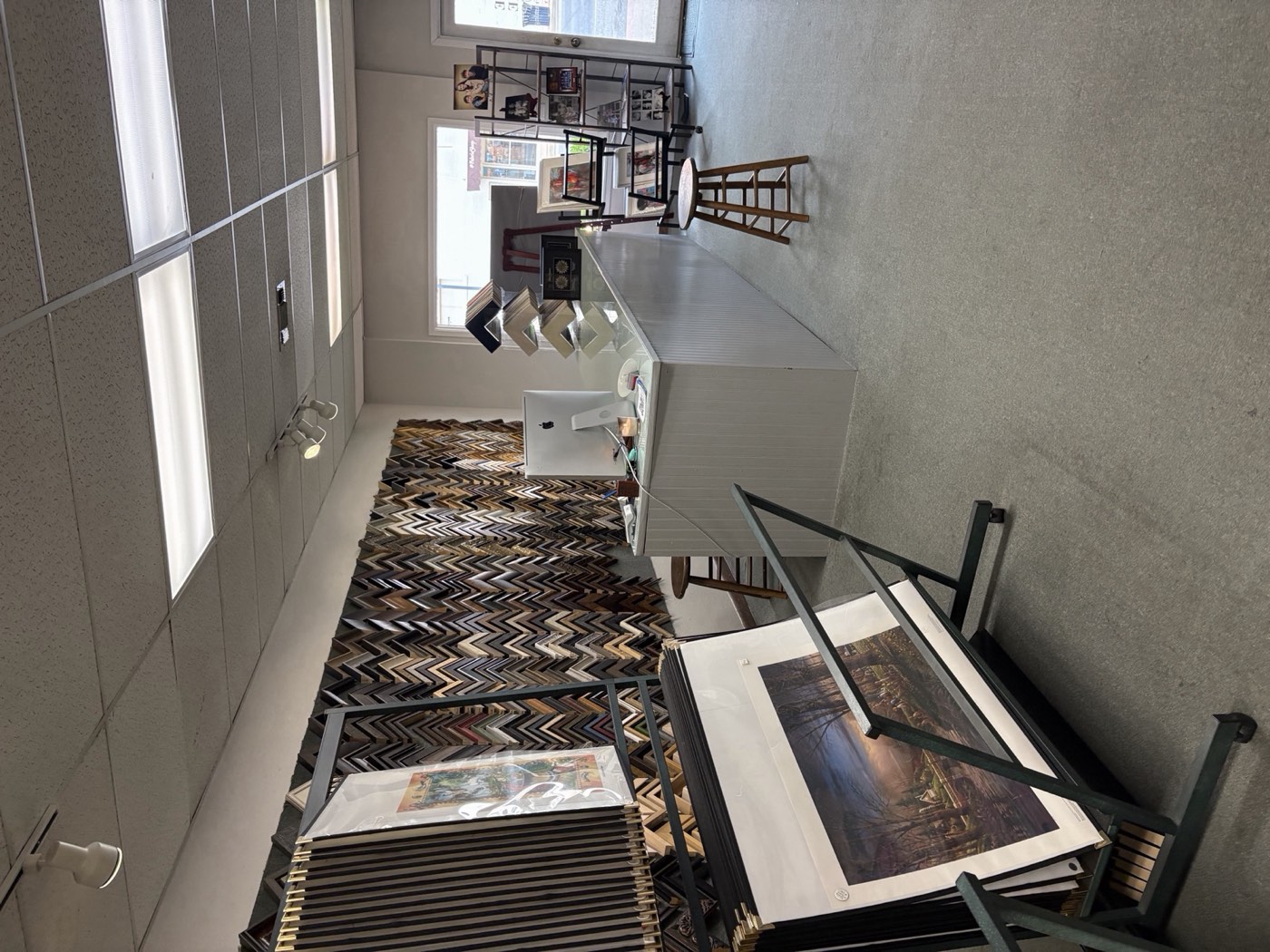 Inside The Frame Up — print rack in foreground, moulding wall, counter, and daylight from the front window