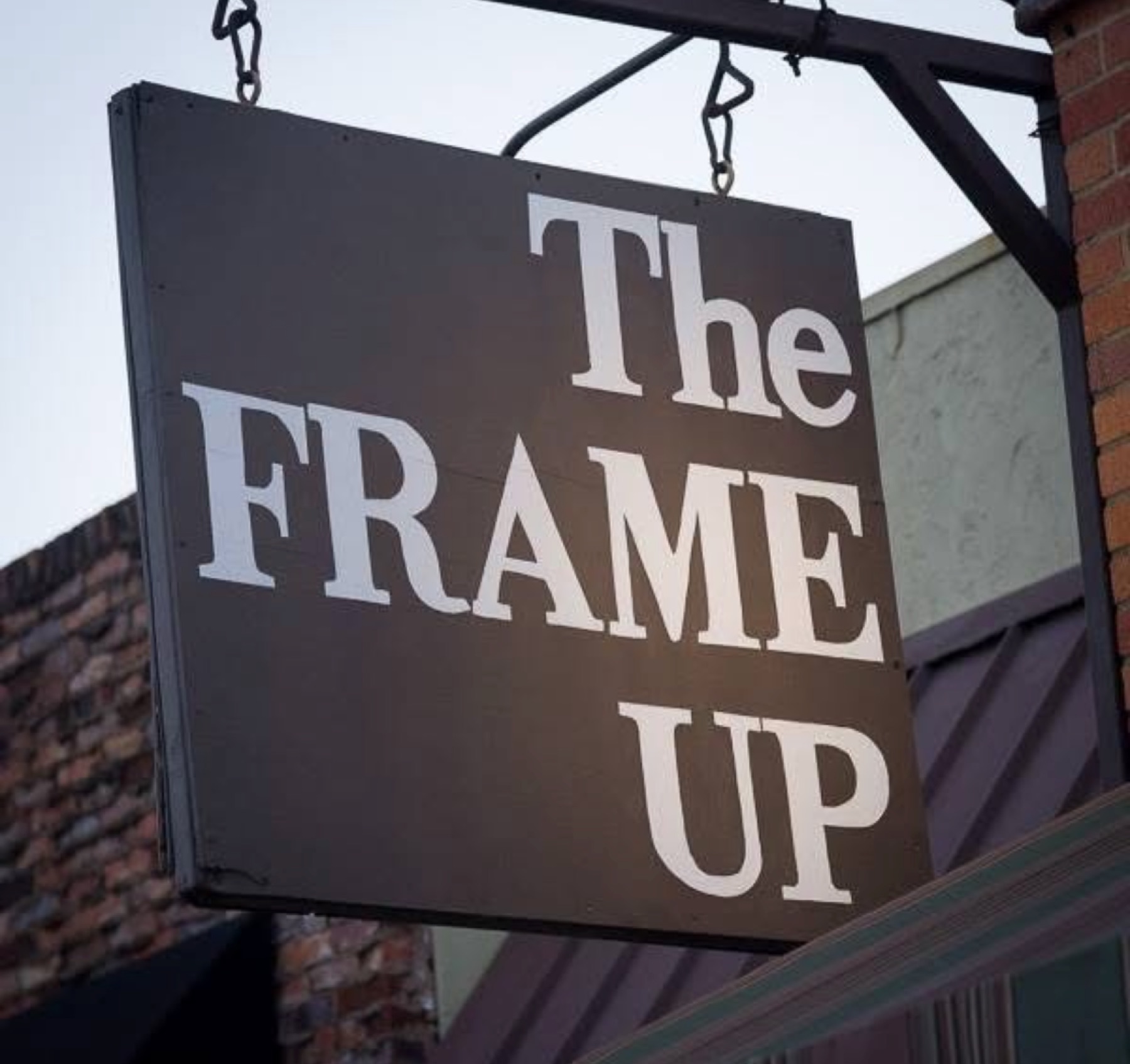 The Frame Up storefront sign hanging on red brick on Vienna Street in downtown Ruston, Louisiana